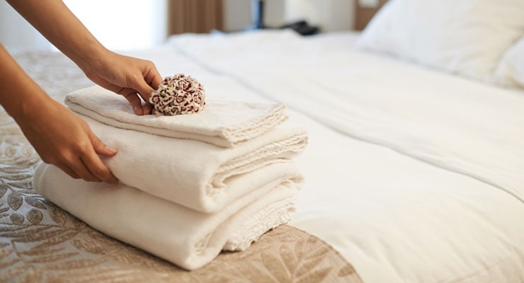 hotel housekeeper setting clean towels on a clean hotel bed