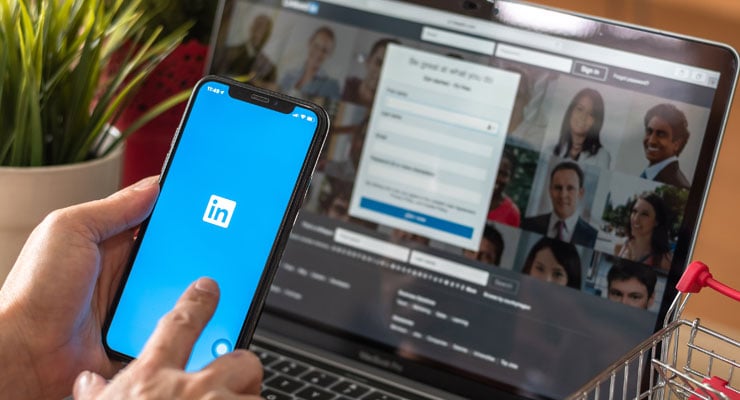 a professional using linkedin app on a phone in front of a laptop with linkedin