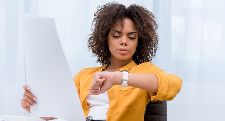 Female employee looking at her watch trying to manage her time to drive process improvement on a work project.