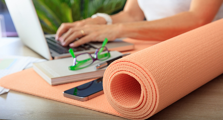 An employee working at a desk next to a rolled up yoga mat.