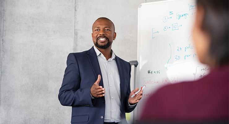 African American man standing in front of whiteboard discussing the importance of improving corporate training programs.