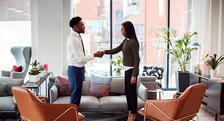 A male and a female shaking hands in an office before meeting to discuss human resources career paths.