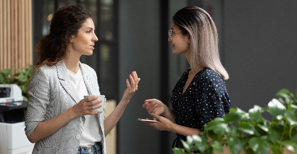 Two female coworkers facing each other discussing strategies for effective communication.	